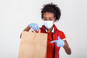 Delivery woman holding paper bag in medical rubber gloves and maskshowing thumb up. copy space. Fast and free Delivery transport . Online shopping and Express delivery . Quarantine photo