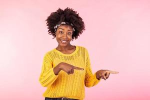 Horizontal shot pleased dark skinned female with Afro haircut, points right with both fore fingers, shows blank space for your promotion, isolated over pink background. People, advertisement concept photo