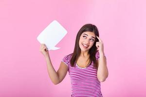 Hey, great idea. Happy pensive beautiful girl looking at blank speech bubble with finger pointing to her head, copy space photo