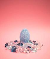 Blue easter egg in a sunset of pink background laying on  blue and white transparent crystals photo