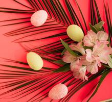 Easter arrangement with pink lilly flowers, pastel easter eggs and green palm leaves. Flat lay on a dark pink background photo