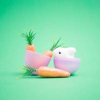 Little white bunny in a purple egg shell with carrots on a green background photo