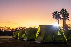 A view of a green canvas camping tent illuminated by floodlights set up on the lawn. photo