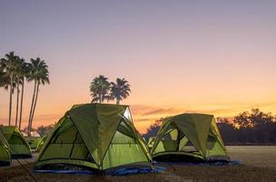 A view of a green canvas camping tent illuminated by floodlights set up on the lawn. photo