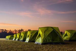 Scenery of rows of green canvas camping tents with floodlights installed on the lawn. photo