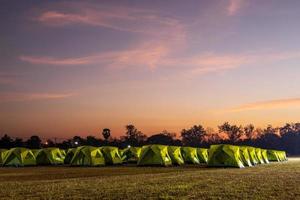 Scenery of rows of green canvas camping tents with floodlights installed on the lawn. photo