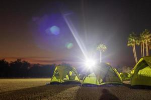 A view of a green canvas camping tent illuminated by floodlights set up on the lawn. photo