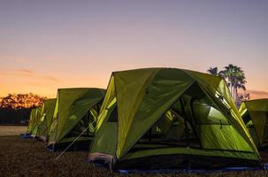 Scenery of rows of green canvas camping tents with floodlights installed on the lawn. photo