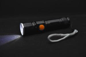 Metal black flashlight on a black background. Burning pocket flashlight close-up. Lighting device. photo