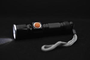 Metal black flashlight on a black background. Burning pocket flashlight close-up. Lighting device. photo