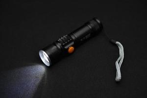 Metal black flashlight on a black background. Burning pocket flashlight close-up. Lighting device. photo