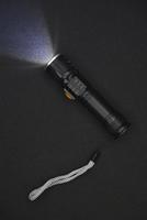 Metal black flashlight on a black background. Burning pocket flashlight close-up. Lighting device. photo