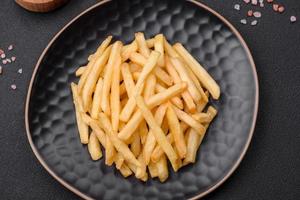 Delicious crispy french fries with salt and spices on a dark concrete background photo