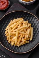 Delicious crispy french fries with salt and spices on a dark concrete background photo