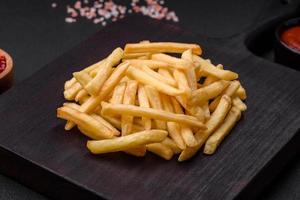 delicioso crujiente francés papas fritas con sal y especias en un oscuro hormigón antecedentes foto