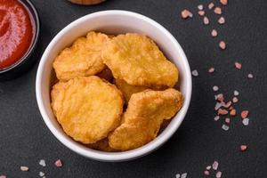 Delicious crispy chicken nuggets with salt and spices on a dark concrete background photo