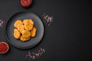 Delicious crispy chicken nuggets with salt and spices on a dark concrete background photo
