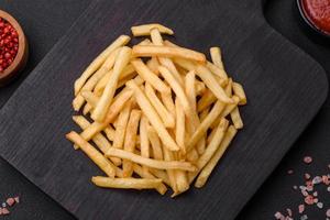 Delicious crispy french fries with salt and spices on a dark concrete background photo