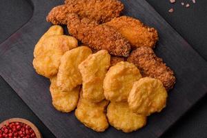 Delicious crispy chicken nuggets with salt and spices on a dark concrete background photo