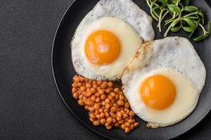 delicioso abundante desayuno consistente de dos frito huevos, Enlatado lentejas y microgreens foto