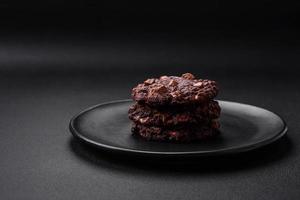 Delicious fresh oatmeal round cookies with chocolate on a black ceramic plate photo