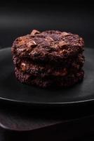 Delicious fresh oatmeal round cookies with chocolate on a black ceramic plate photo