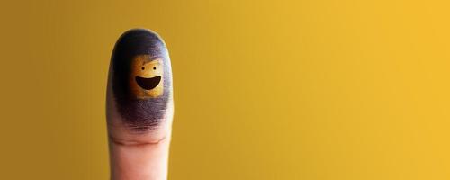 Happiness Day Concept. Happy and Positive Mind, Well Mental Health. Enjoying Life Everyday. Smiling Face on Thumb against Yellow Wall photo
