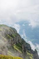 A steep cliff overgrown with grass and hidden by clouds photo