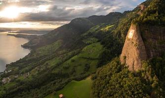 a huge swiss flag is fixed on a cliff, below it is a village on a lake photo