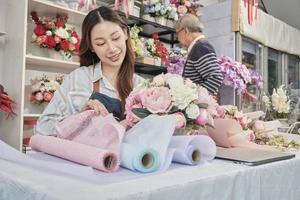 joven y hermosa empresaria asiática de floristería que organiza un ramo de flores trabaja con un anciano comerciante, feliz trabajo en una colorida tienda de flores con flores frescas, pequeñas empresas, pyme familiar. foto