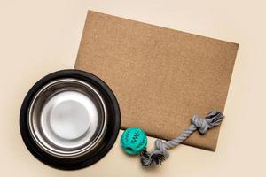 dog bowl for food and toys with blank brown sheet for text on beige background with copy space, pets photo