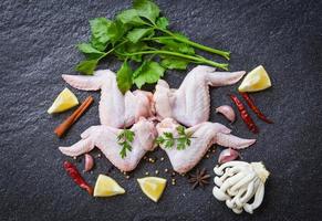 raw chicken wings with lemon chilli herbs and spices and mushroom on black plate  top view - Raw uncooked chicken meat marinated with ingredients for cooking photo