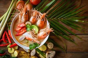 Shrimp soup on seafood soup bowl with thai herb and spices, Hot and sour spicy shrimps prawns soup  curry lemon lime galangal red chili straw mushroom on table food, Thai Food Tom Yum Kung photo