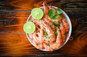 camarón en blanco bolw y de madera antecedentes comida mesa alimento, Fresco camarones langostinos Mariscos limón Lima con hierbas y especia foto