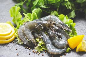 crudo camarones en plato - Fresco camarón langostinos sin cocer con especias limón y vegetal ensalada lechuga o verde roble en oscuro antecedentes en el Mariscos restaurante foto