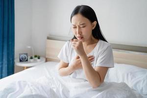 asiático mujer sensación enfermo y tos en cama en el Mañana. respiratorio enfermedades. foto