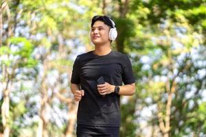 Asian young man running at the park in the morning He listens to his favorite music with wireless headphones. photo