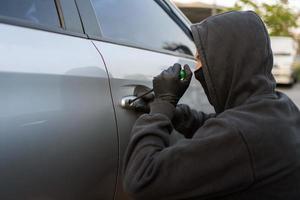 un coche ladrón usa negro guantes y sostiene un destornillador a palanca abierto el coche puerta. foto