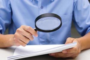 Close up hand of businessperson looking at documents through magnifying glass. Concept of business and data validation. photo