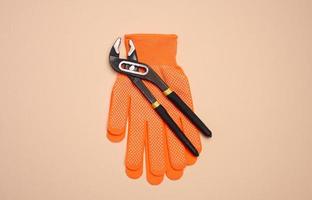 Orange glove and metal universal adjustable wrench on a beige background, top view photo