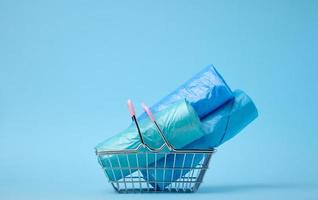 Rolls of plastic bags in a miniature shopping basket on a blue background photo