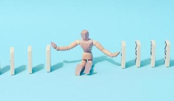 A wooden puppet toy holds back a falling domino on a blue background, representing the concept of a strong personality photo
