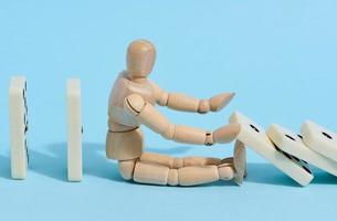 A wooden puppet toy holds back a falling domino on a blue background, representing the concept of a strong personality photo