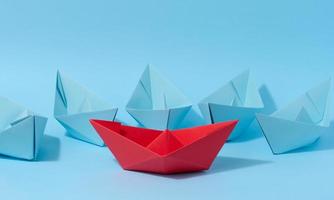 A red paper boat stands in front of a group of blue paper boats, a confrontation photo