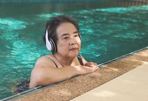 happy and healthy  Asian senior  woman listening to the music with headphones in a pool photo