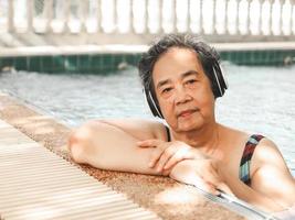 happy and healthy  Asian senior  woman listening to the music with headphones in a pool photo