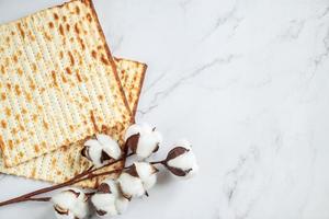 feliz Pascua. fondo religioso fiesta judía pesaj. pan de matzá y flores de algodón sobre un mármol blanco. copie el espacio foto