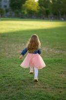 A little girl 3 years old in a summer dress runs away from the camera. The girl is turned back. Summer time. photo