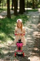 A little girl 3 years old in a pink cap rides a scooter. Summer time.