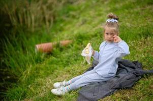 A little girl 3 years old sits in a suit on the grass in the park and eats pizza. photo